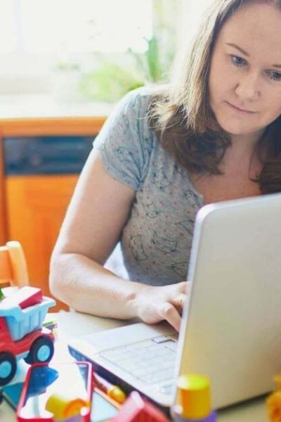 teacher mom working on a laptop with toddler playing with toys