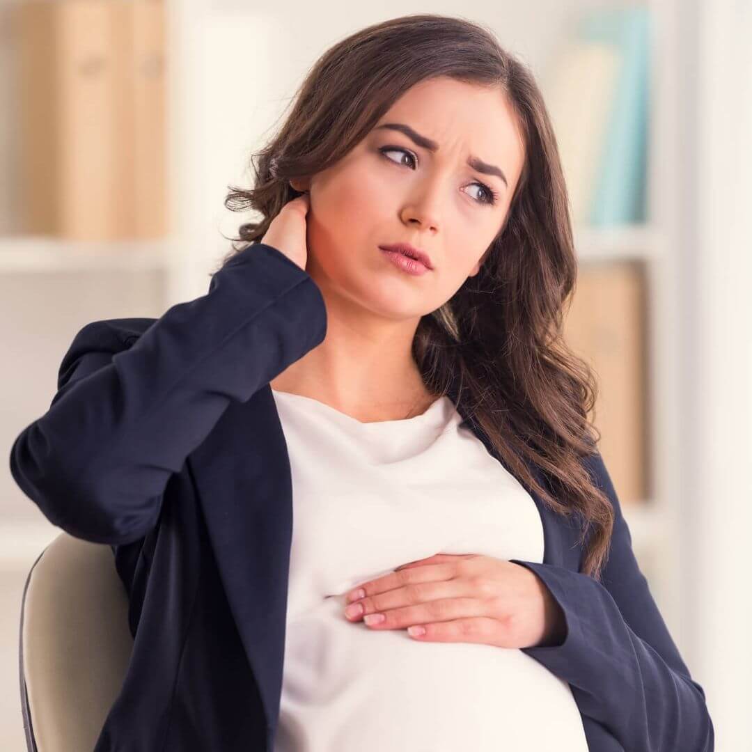 Brunette pregnant woman working at a desk showing she is tired