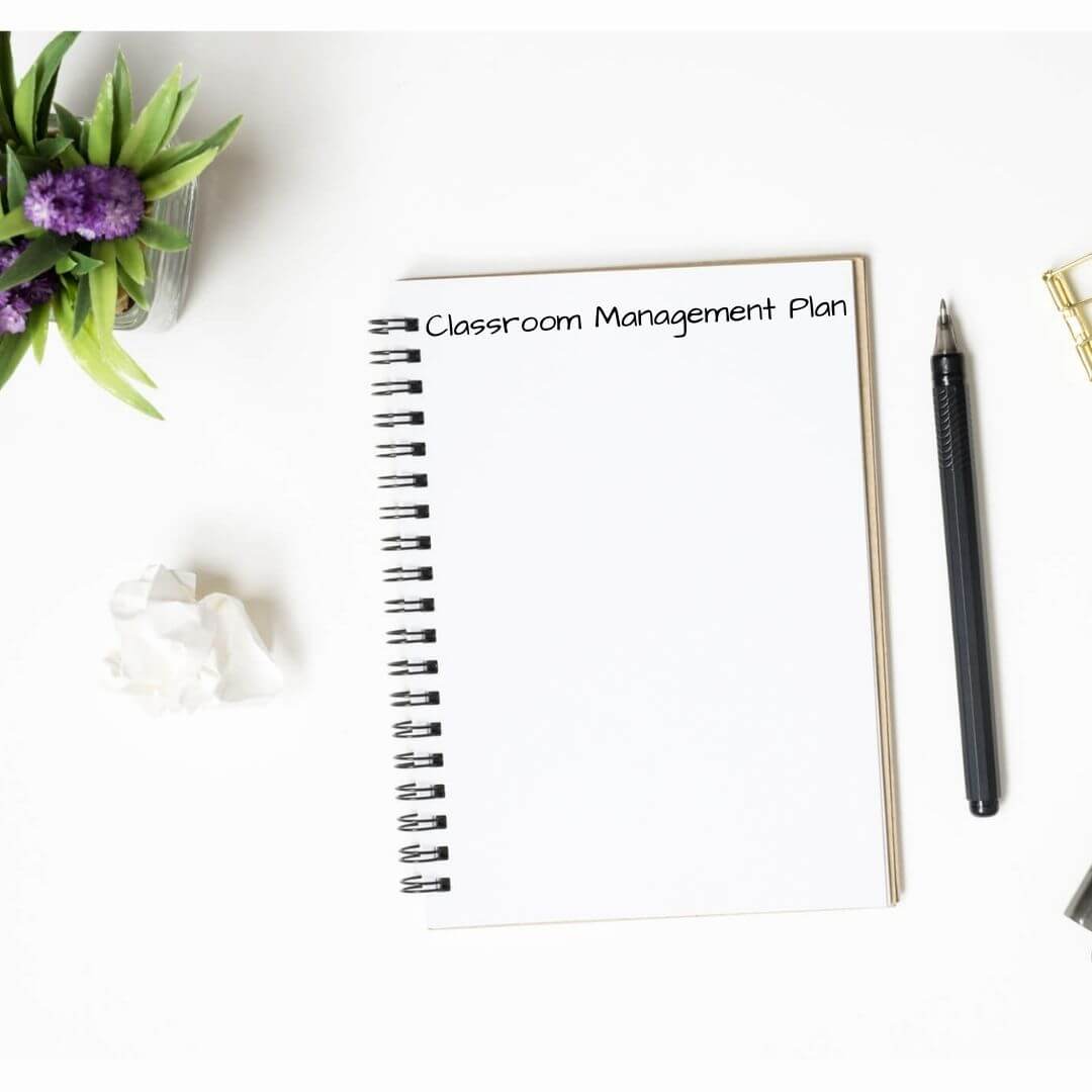 White desk with purple flowers and note book that says Classroom Management Plan at the top