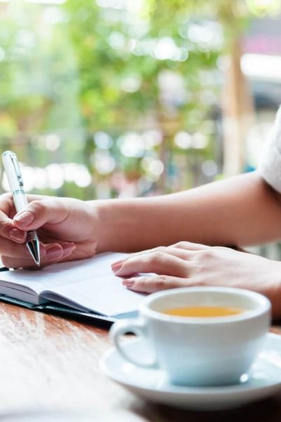 Woman writing in a journal and drinking tea for self care