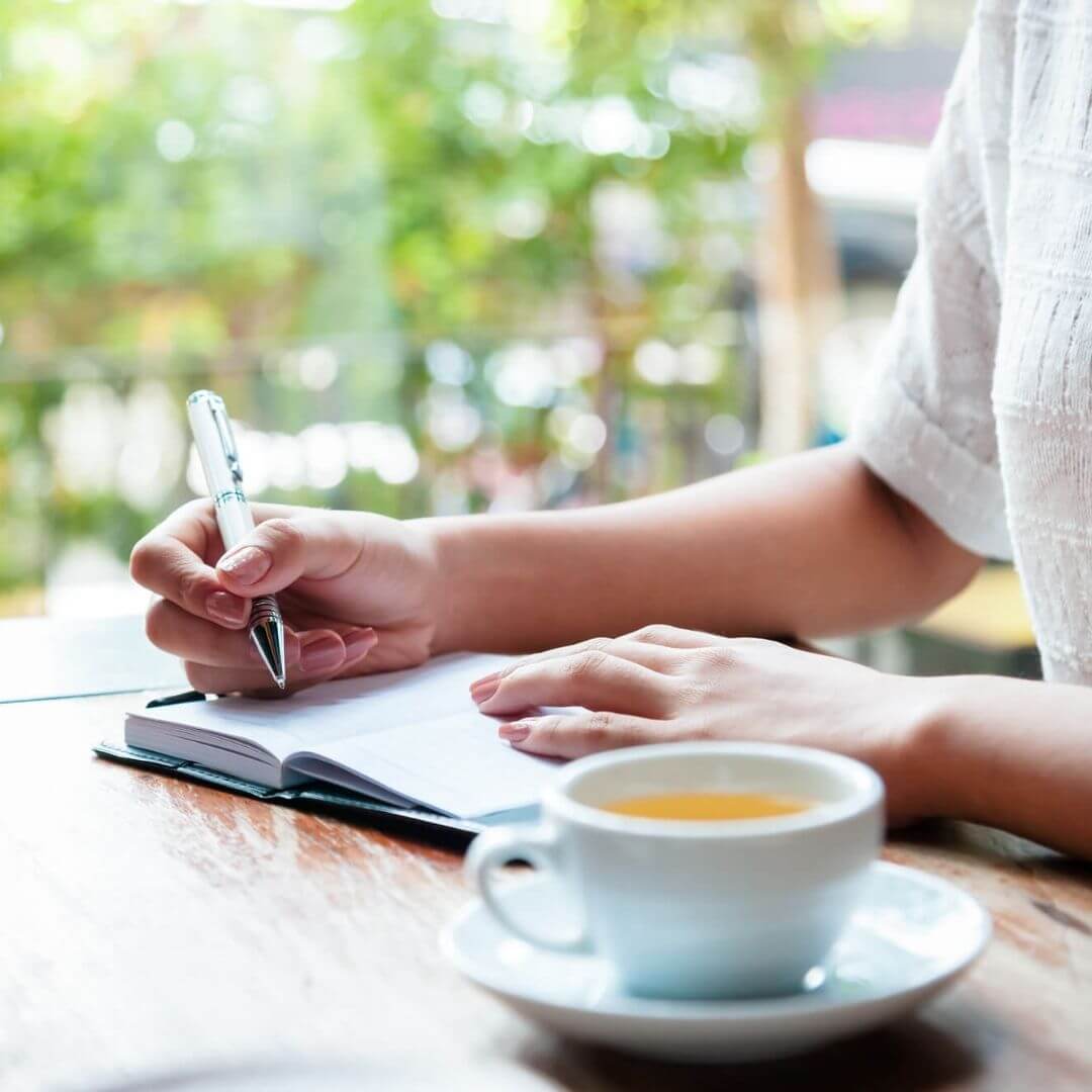 Woman writing in a journal and drinking tea for self care