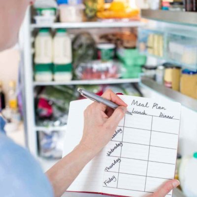 Mom holding a pen and making a meal plan in a notebook in front of an open refrigerator