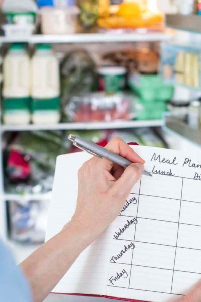 Mom holding a pen and making a meal plan in a notebook in front of an open refrigerator